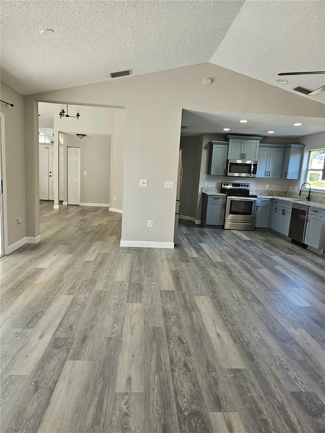 kitchen with stainless steel appliances, vaulted ceiling, hardwood / wood-style flooring, and gray cabinetry