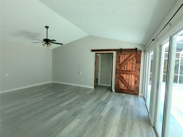 unfurnished living room with ceiling fan, a barn door, light hardwood / wood-style flooring, a textured ceiling, and lofted ceiling