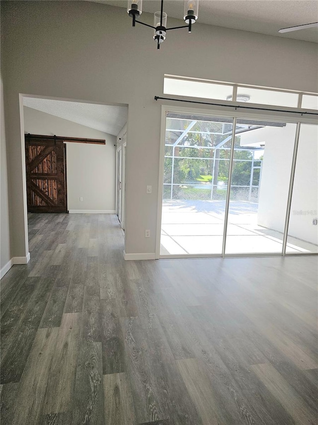 unfurnished living room featuring hardwood / wood-style floors, a barn door, and vaulted ceiling