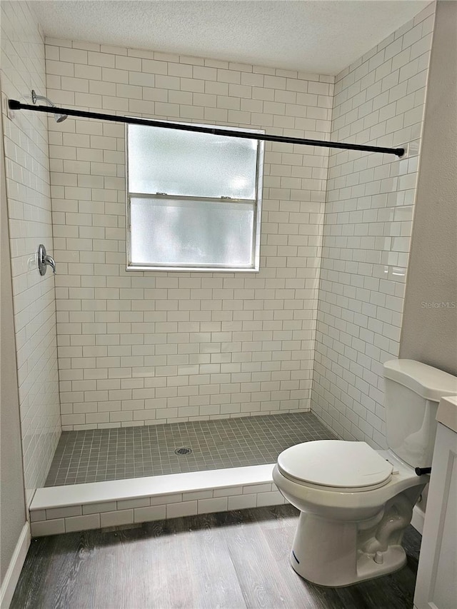 bathroom featuring tiled shower, wood-type flooring, a textured ceiling, and toilet