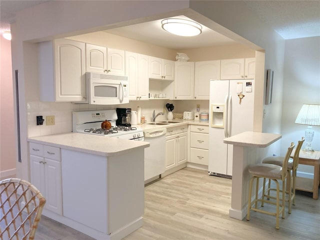 kitchen with white appliances, sink, kitchen peninsula, light hardwood / wood-style flooring, and white cabinetry