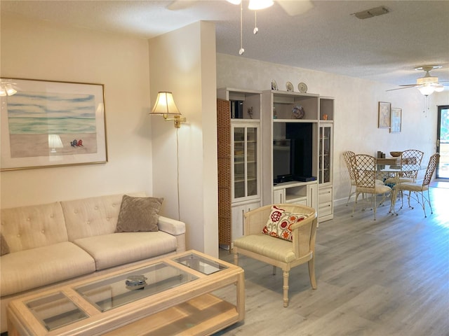 living room featuring ceiling fan, wood-type flooring, and a textured ceiling