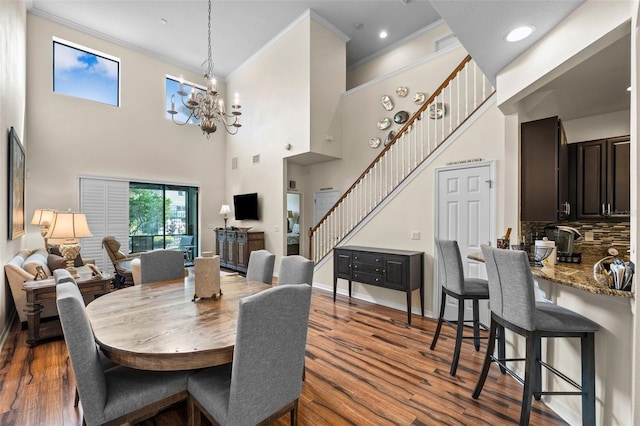 dining space featuring wood-type flooring, ornamental molding, a towering ceiling, and an inviting chandelier