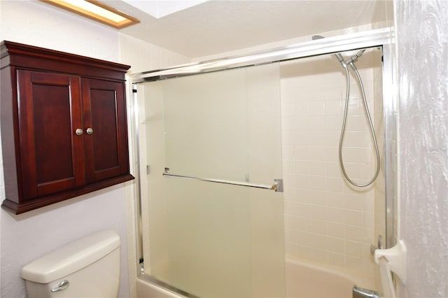 bathroom featuring toilet and bath / shower combo with glass door