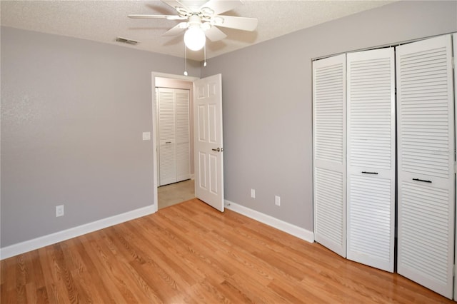 unfurnished bedroom with ceiling fan, a closet, light wood-type flooring, and a textured ceiling