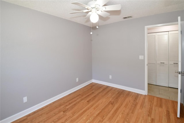 unfurnished bedroom featuring ceiling fan, a textured ceiling, a closet, and light hardwood / wood-style flooring