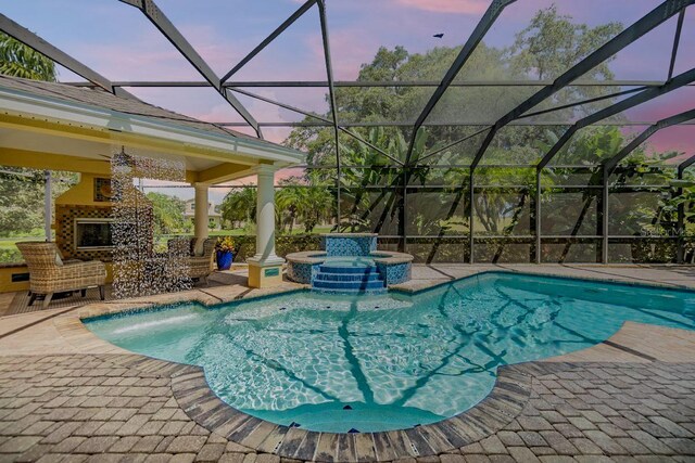 pool at dusk featuring a lanai and an in ground hot tub