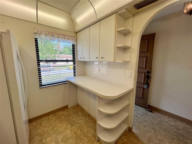 kitchen with arched walkways, open shelves, light countertops, decorative backsplash, and freestanding refrigerator