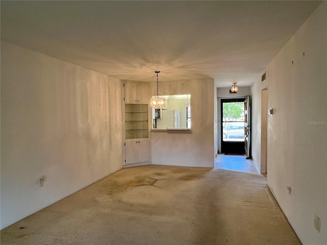 unfurnished living room with carpet flooring, built in shelves, and an inviting chandelier