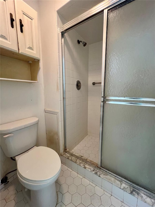 bathroom featuring tile flooring, a shower with shower door, and toilet