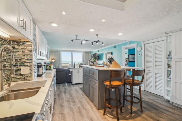 kitchen with light wood finished floors, a kitchen breakfast bar, a center island, a textured ceiling, and a sink