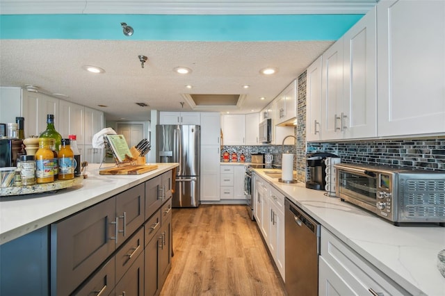 kitchen featuring stainless steel appliances, a toaster, white cabinets, and light wood finished floors