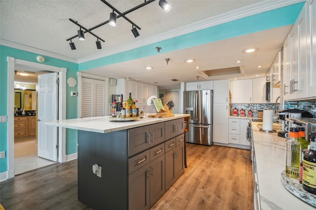 kitchen featuring white cabinetry, a center island, stainless steel refrigerator with ice dispenser, backsplash, and crown molding