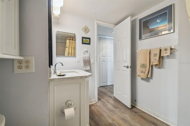 full bath with baseboards, a textured ceiling, vanity, and wood finished floors