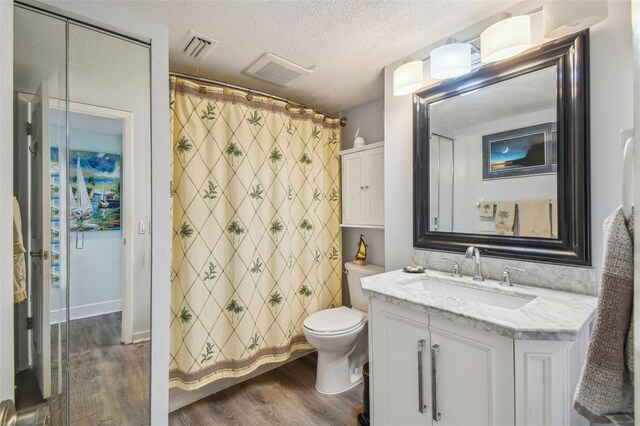 full bathroom with visible vents, toilet, vanity, a textured ceiling, and wood finished floors