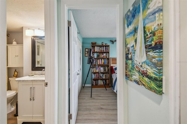 hallway with a textured ceiling, light wood-type flooring, and a sink