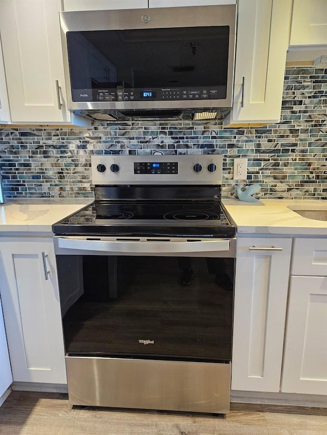 6035 Sea Ranch Dr Unit 505, Hudson, FL 34667 - kitchen view of appliances with stainless steel finishes, white cabinetry, decorative backsplash, light wood-style flooring, and light stone countertops