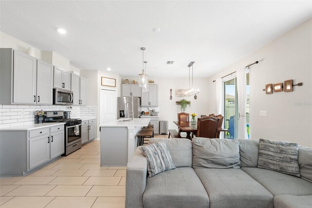 kitchen with a center island with sink, hanging light fixtures, decorative backsplash, gray cabinets, and appliances with stainless steel finishes