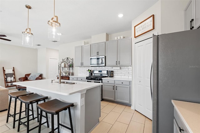 kitchen with decorative backsplash, appliances with stainless steel finishes, gray cabinetry, a center island with sink, and hanging light fixtures