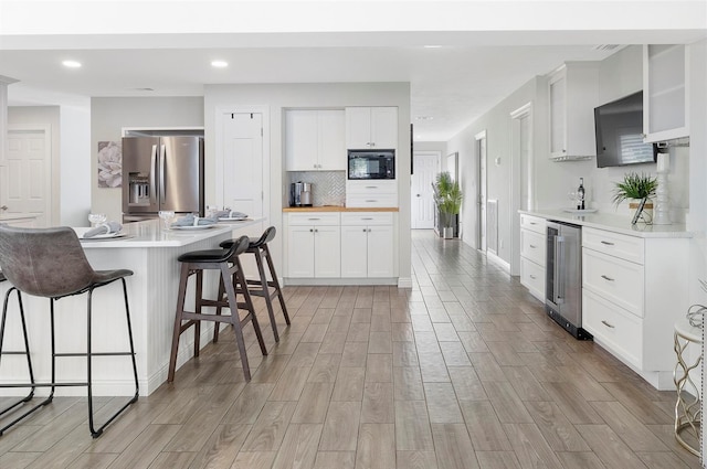 kitchen with backsplash, white cabinets, stainless steel refrigerator with ice dispenser, black microwave, and beverage cooler