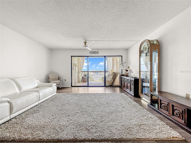 living room featuring dark wood-type flooring, ceiling fan, and a textured ceiling