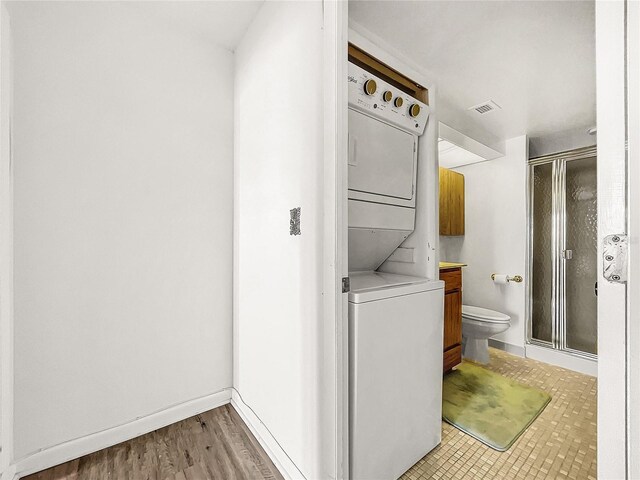 bathroom with a shower with door, vanity, stacked washer / drying machine, and toilet