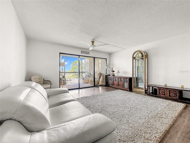 living room featuring wood-type flooring, a textured ceiling, and ceiling fan