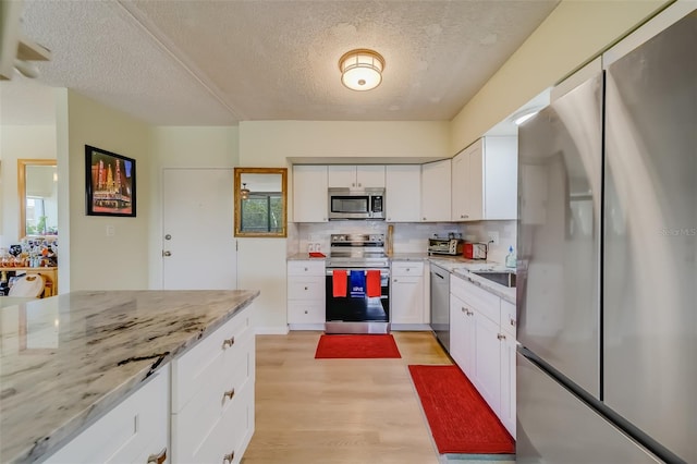 kitchen with appliances with stainless steel finishes, light stone counters, a textured ceiling, light hardwood / wood-style floors, and white cabinetry