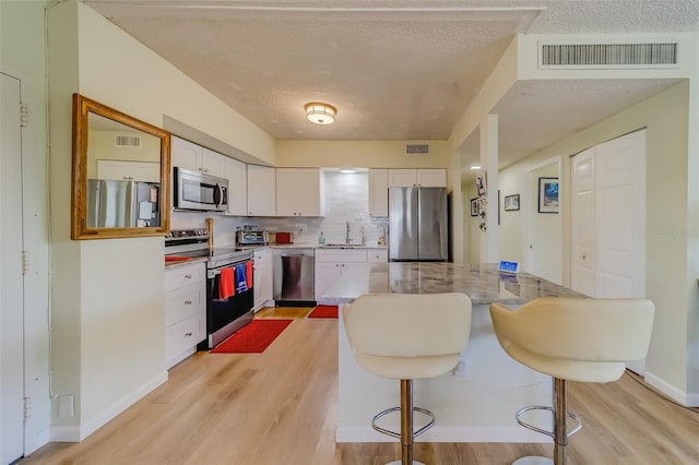 kitchen featuring appliances with stainless steel finishes, backsplash, sink, light hardwood / wood-style flooring, and white cabinets