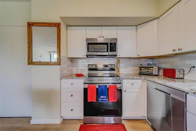 kitchen featuring decorative backsplash, appliances with stainless steel finishes, white cabinetry, and light stone countertops