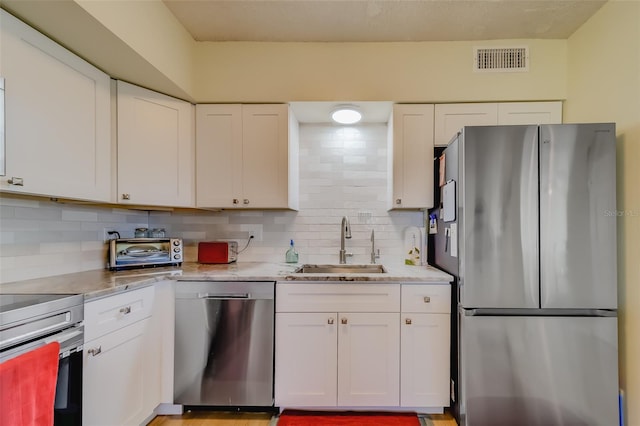 kitchen featuring stainless steel appliances, white cabinetry, tasteful backsplash, and sink