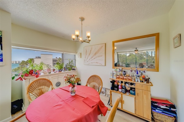 dining room with ceiling fan with notable chandelier, light wood-type flooring, and a textured ceiling