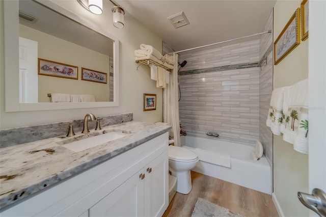 full bathroom with hardwood / wood-style floors, vanity, tiled shower / bath combo, and toilet