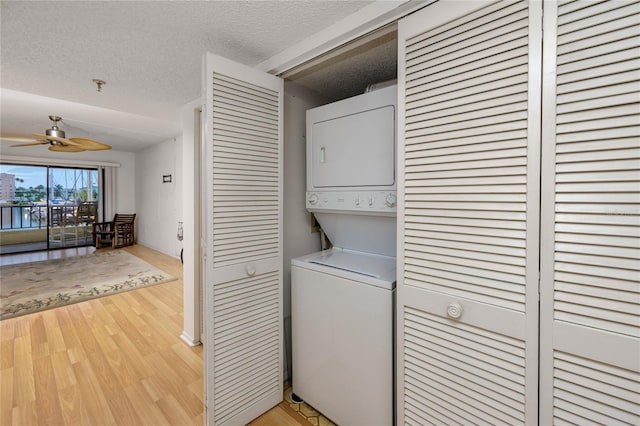 clothes washing area with stacked washer / drying machine, ceiling fan, a textured ceiling, and light hardwood / wood-style flooring