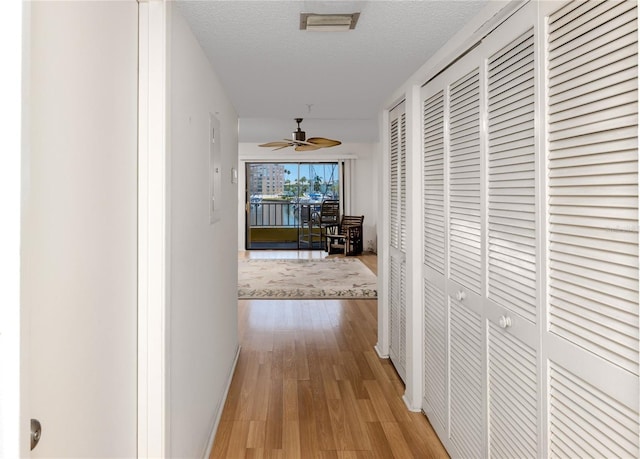 hallway with a textured ceiling and light hardwood / wood-style flooring