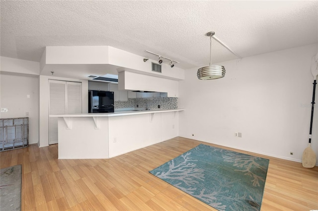 kitchen featuring white cabinetry, kitchen peninsula, backsplash, decorative light fixtures, and a kitchen breakfast bar