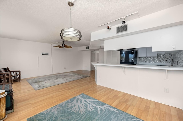 kitchen with kitchen peninsula, black refrigerator, light wood-type flooring, a textured ceiling, and a breakfast bar