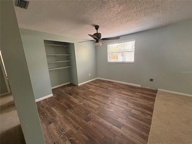 unfurnished bedroom with ceiling fan, a closet, dark wood-type flooring, and a textured ceiling