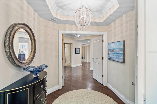 corridor with a chandelier, dark hardwood / wood-style flooring, a tray ceiling, and crown molding