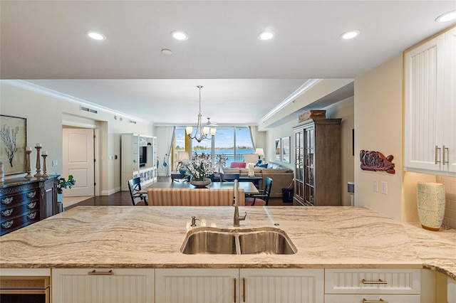 kitchen with light stone countertops, crown molding, sink, decorative light fixtures, and an inviting chandelier