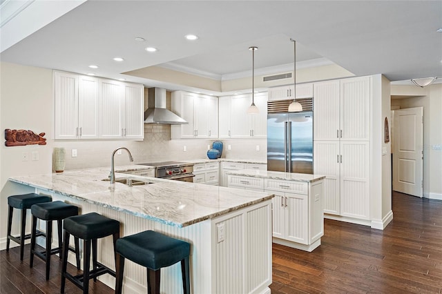 kitchen featuring pendant lighting, wall chimney range hood, sink, premium appliances, and kitchen peninsula