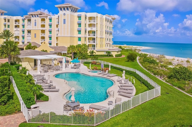 view of pool with a lawn, a patio area, a water view, and a beach view