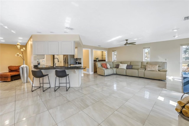 kitchen with ceiling fan, sink, light tile patterned flooring, white cabinetry, and a kitchen breakfast bar