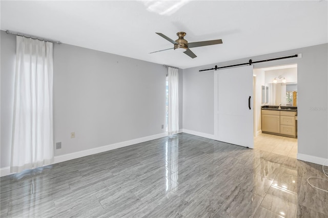 spare room featuring ceiling fan, sink, and a barn door