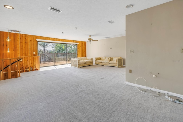 unfurnished living room featuring carpet floors, a textured ceiling, wood walls, and ceiling fan