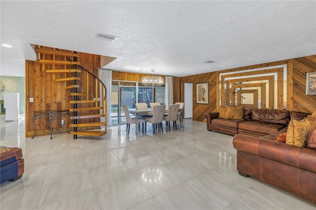 tiled living room with a textured ceiling, an inviting chandelier, and wooden walls