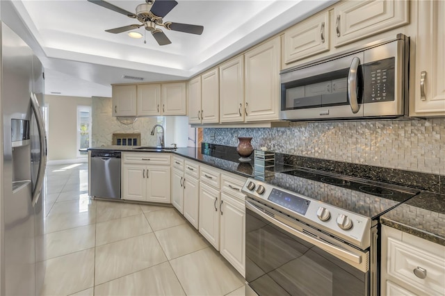 kitchen featuring backsplash, sink, light tile patterned flooring, stainless steel appliances, and dark stone counters