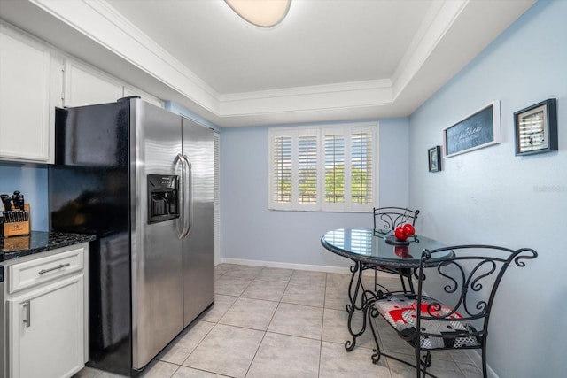 kitchen featuring a raised ceiling, dark stone countertops, stainless steel fridge, crown molding, and white cabinets