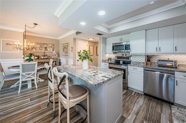 kitchen with white cabinetry, a kitchen island, hanging light fixtures, and appliances with stainless steel finishes