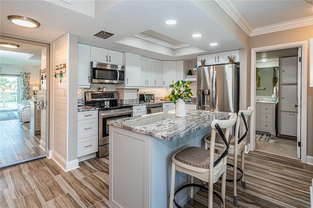 kitchen featuring white cabinetry, a center island, crown molding, decorative backsplash, and appliances with stainless steel finishes